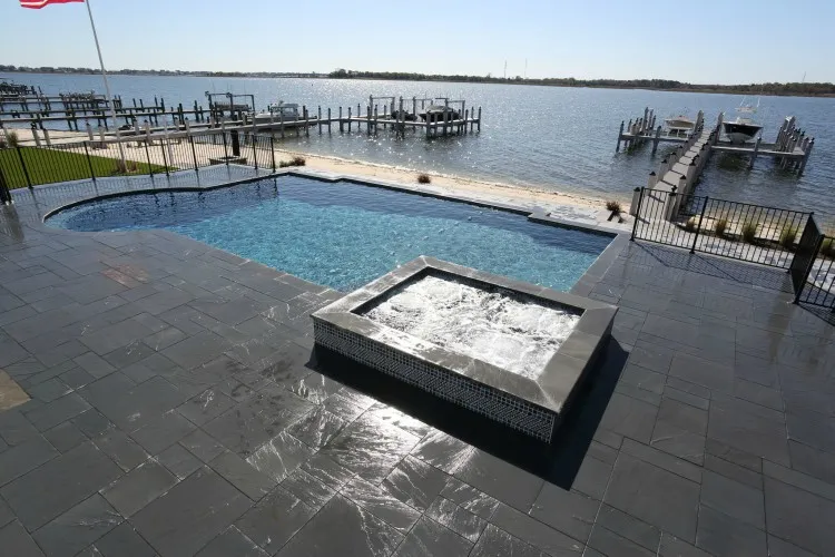 Geometric pool with raised square glass tile spa and dark slate paver deck overlooking a waterfront marina in Lakehurst, NJ by Gorlin Pools