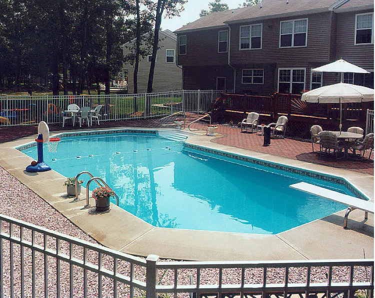 Rectangular pool with diving board, floating basketball hoop, white metal fence, and brick paver patio at a suburban home in Lakehurst, NJ by Gorlin Pools