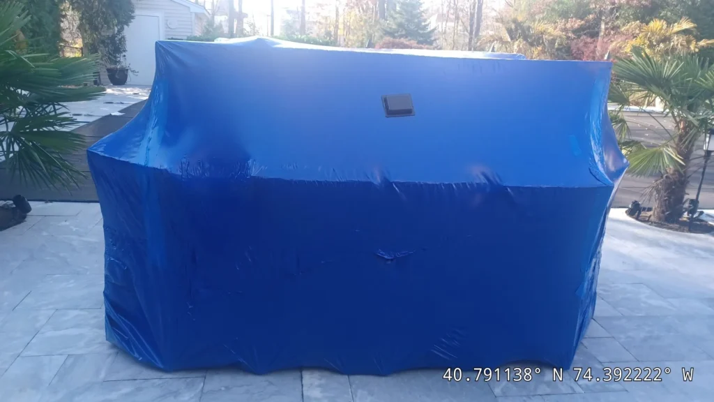 Blue shrink wrap cover over an outdoor kitchen on a stone patio for winter protection in Lakehurst, NJ by Gorlin Pools