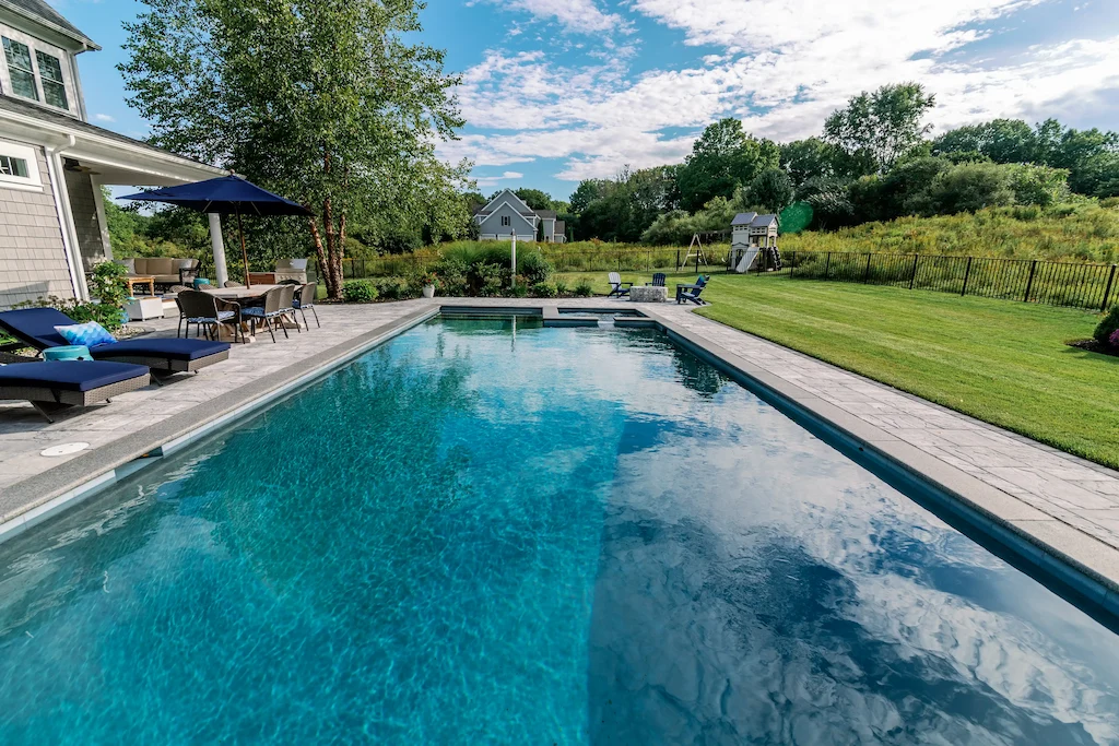 Rectangular pool with raised spa spillover, stamped concrete deck, and outdoor dining area in Lakehurst, NJ by Gorlin Pools