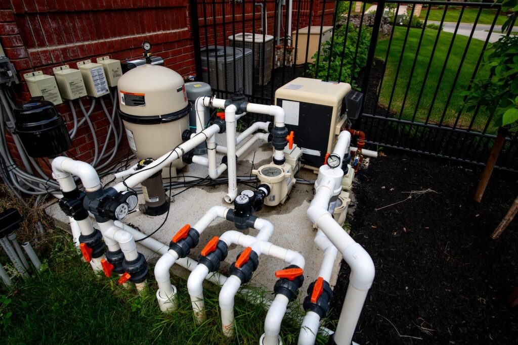 A clean, realistic photograph of a modern pool heater system installed beside a pristine swimming pool